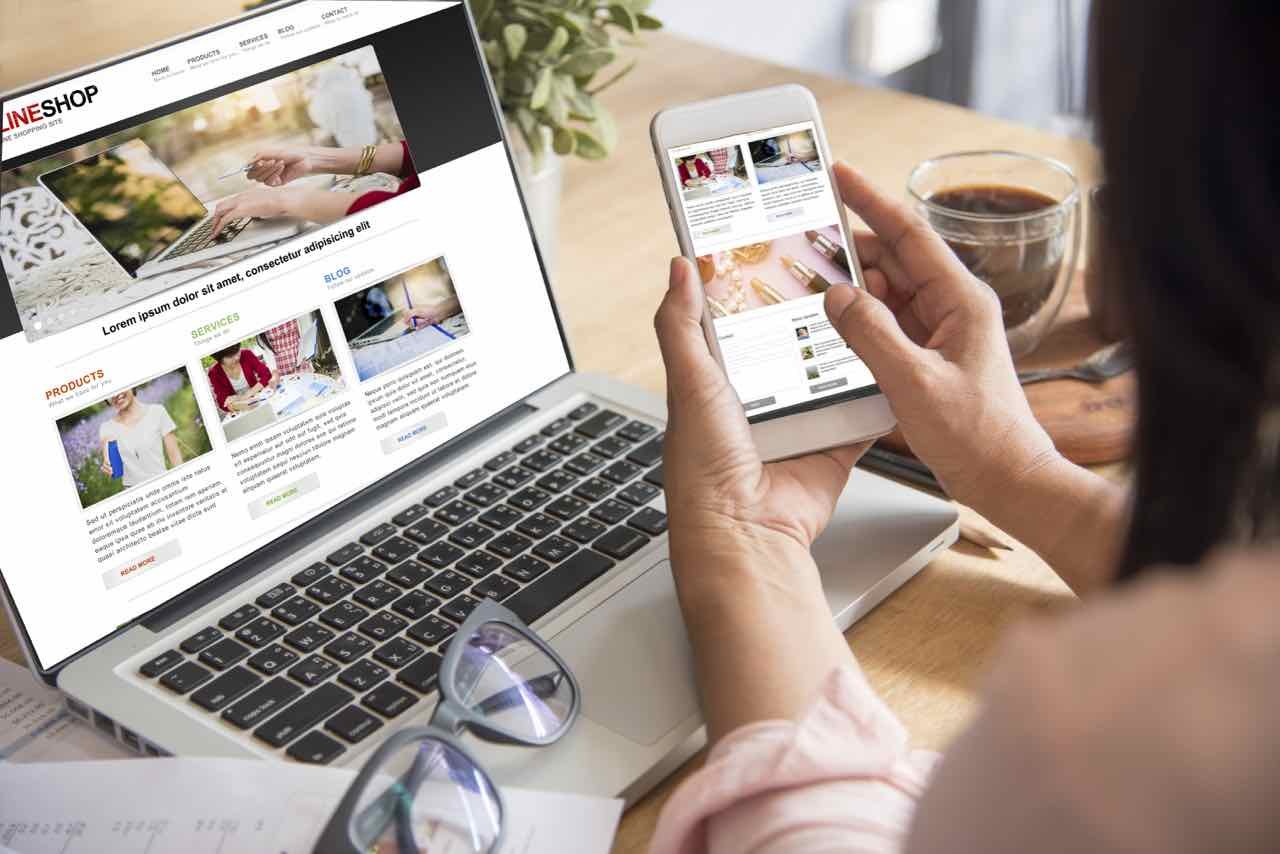 A shopper researching a product on a laptop while comparing notes, prices and features before buying